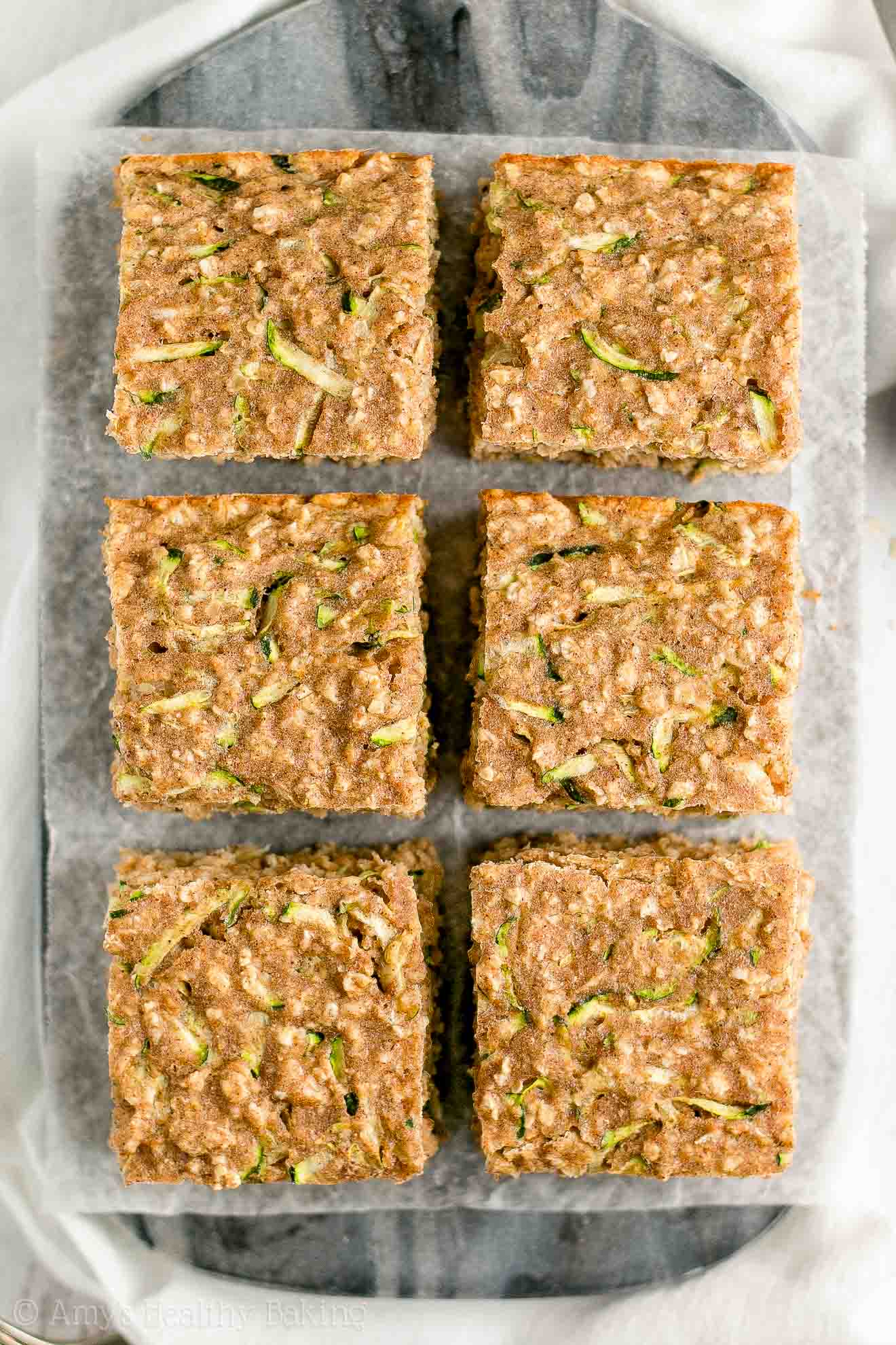 six square slices of healthy zucchini oatmeal snack cake arranged in two rows of three on a dark marble serving tray – easy recipe for a healthy zucchini cake full of oats and spices – low calorie, low fat, soft, moist, and clean eating with whole wheat and gluten free options – made with greek yogurt, pure maple syrup, and no refined sugar
