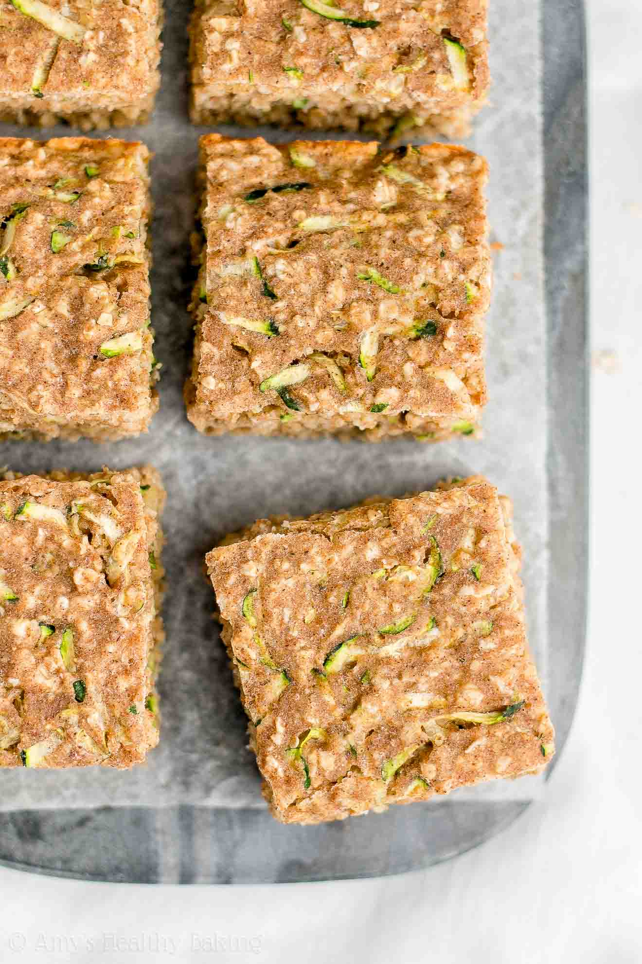 square slices of healthy zucchini oatmeal snack cake arranged on a dark marble serving tray lined with white parchment paper – easy recipe for a healthy zucchini cake full of oats and spices – low calorie, low fat, soft, moist, and clean eating with whole wheat and gluten free options – made with greek yogurt, pure maple syrup, and no refined sugar
