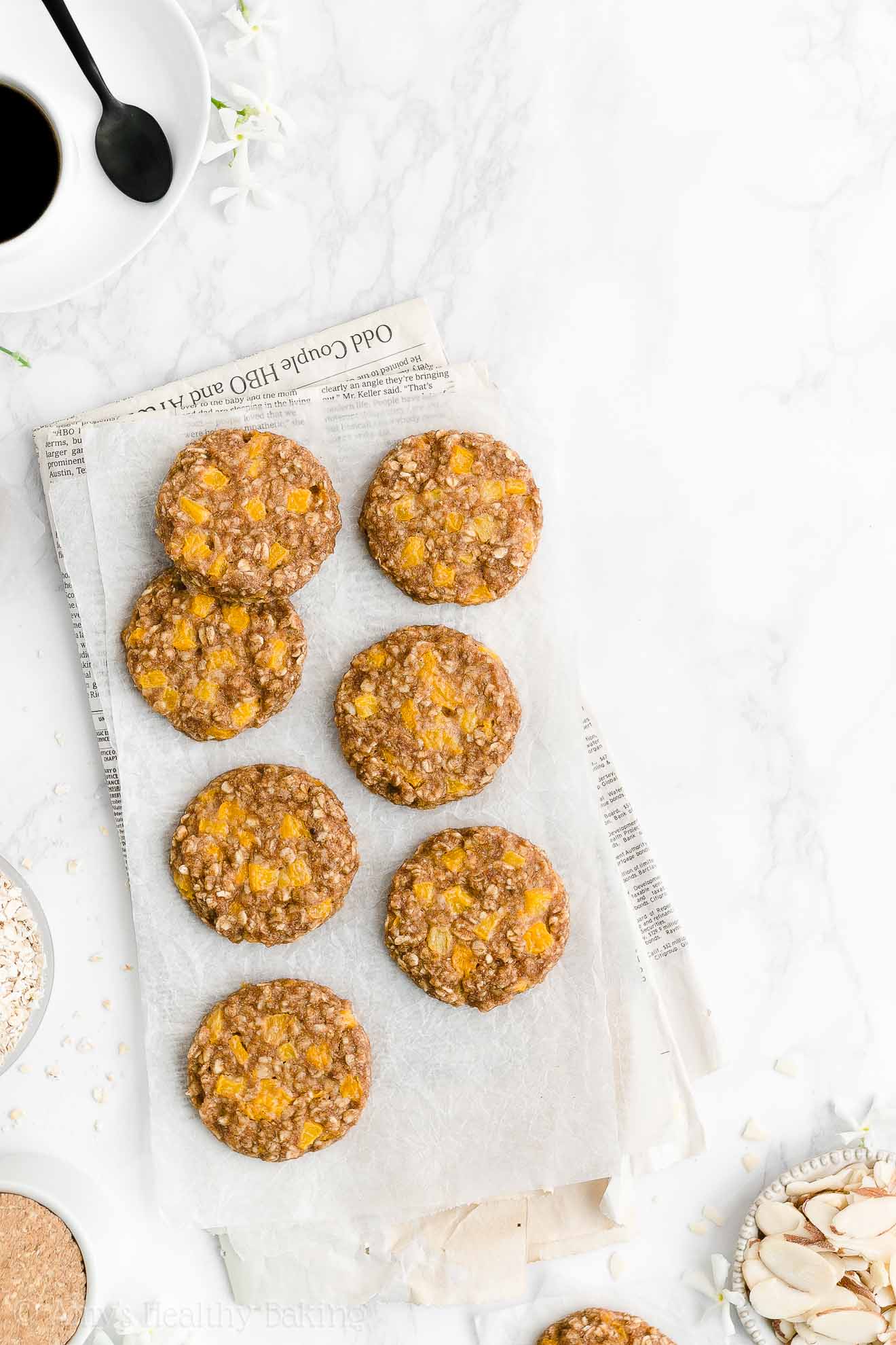 seven of the best healthy peach oatmeal breakfast cookies arranged on white parchment paper sitting on top of a folded newspaper – easy fruit and oat breakfast cookie recipe – soft, chewy, low calorie, low fat, dairy free, and clean eating with whole wheat and gluten free options – made with oats, spices, pure maple syrup, fresh peaches or canned peaches, and no refined sugar