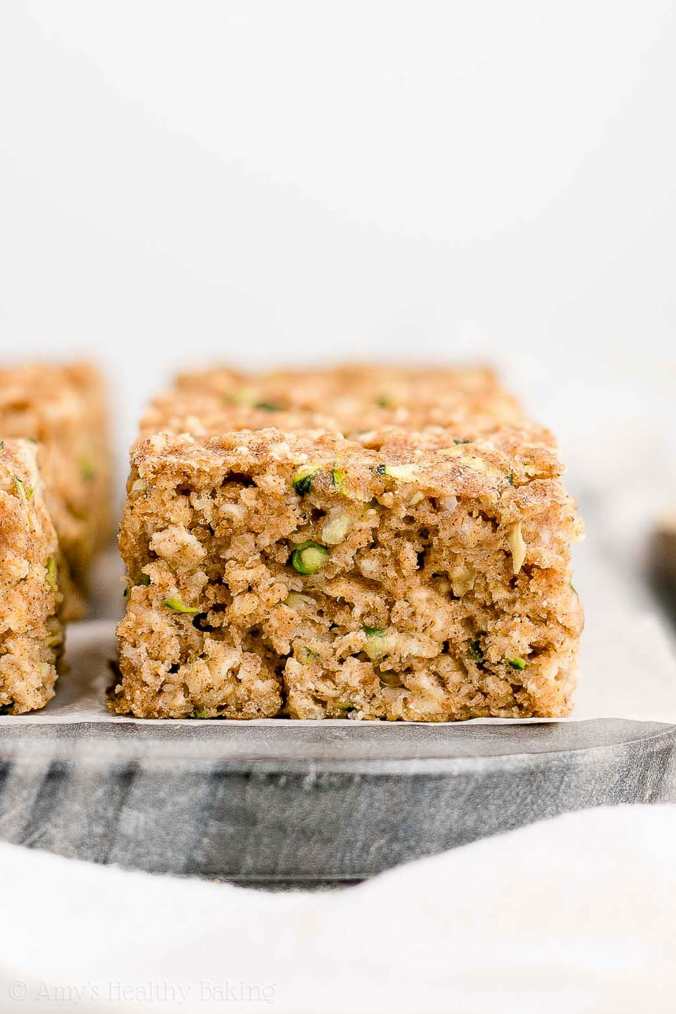 square slices of healthy zucchini oatmeal snack cake on a dark marble serving tray – easy recipe for a healthy zucchini cake full of oats and spices – low calorie, low fat, soft, moist, and clean eating with whole wheat and gluten free options – made with greek yogurt, pure maple syrup, and no refined sugar