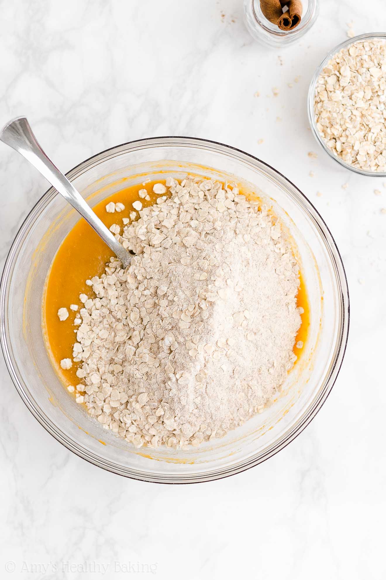 glass mixing bowl holding a fork and the wet ingredients used to make healthy pumpkin oatmeal bars, with the dry ingredients poured in a mound on top – easy oat bars recipe for breakfasts and snacks – vegan, gluten free, egg free, dairy free, and clean eating with whole wheat and gluten free options – made with oats, pumpkin, spices, and no refined sugar