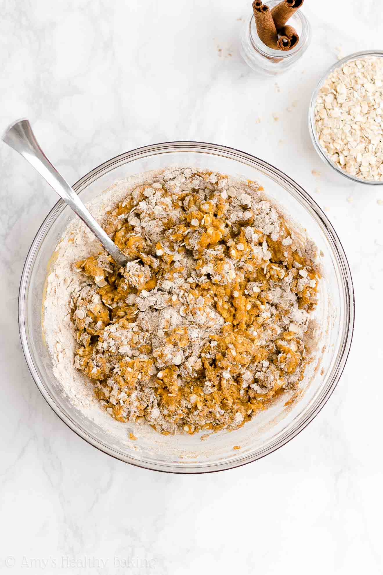 glass mixing bowl holding a fork and the partially stirred mixture used to make healthy pumpkin oatmeal bars – easy oat bars recipe for breakfasts and snacks – vegan, gluten free, egg free, dairy free, and clean eating with whole wheat and gluten free options – made with oats, pumpkin, spices, and no refined sugar