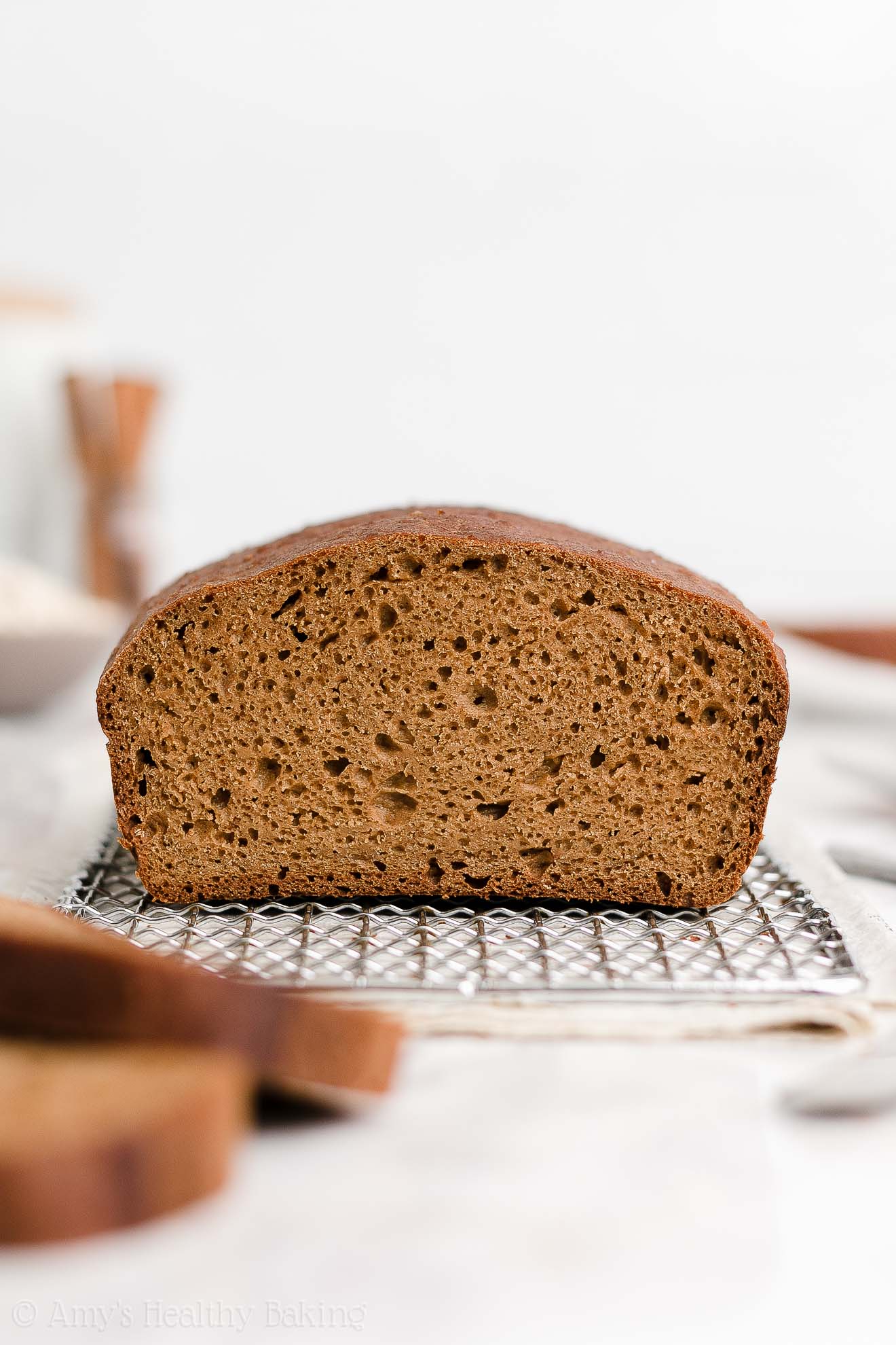 a healthy oatmeal gingerbread loaf sitting on a wire cooling rack with two slices off to the left in the foreground – easy gingerbread quick bread recipe – soft, moist, low fat, low calorie, and clean eating with whole wheat and gluten free options – made with oats, Greek yogurt, molasses, and no refined sugar
