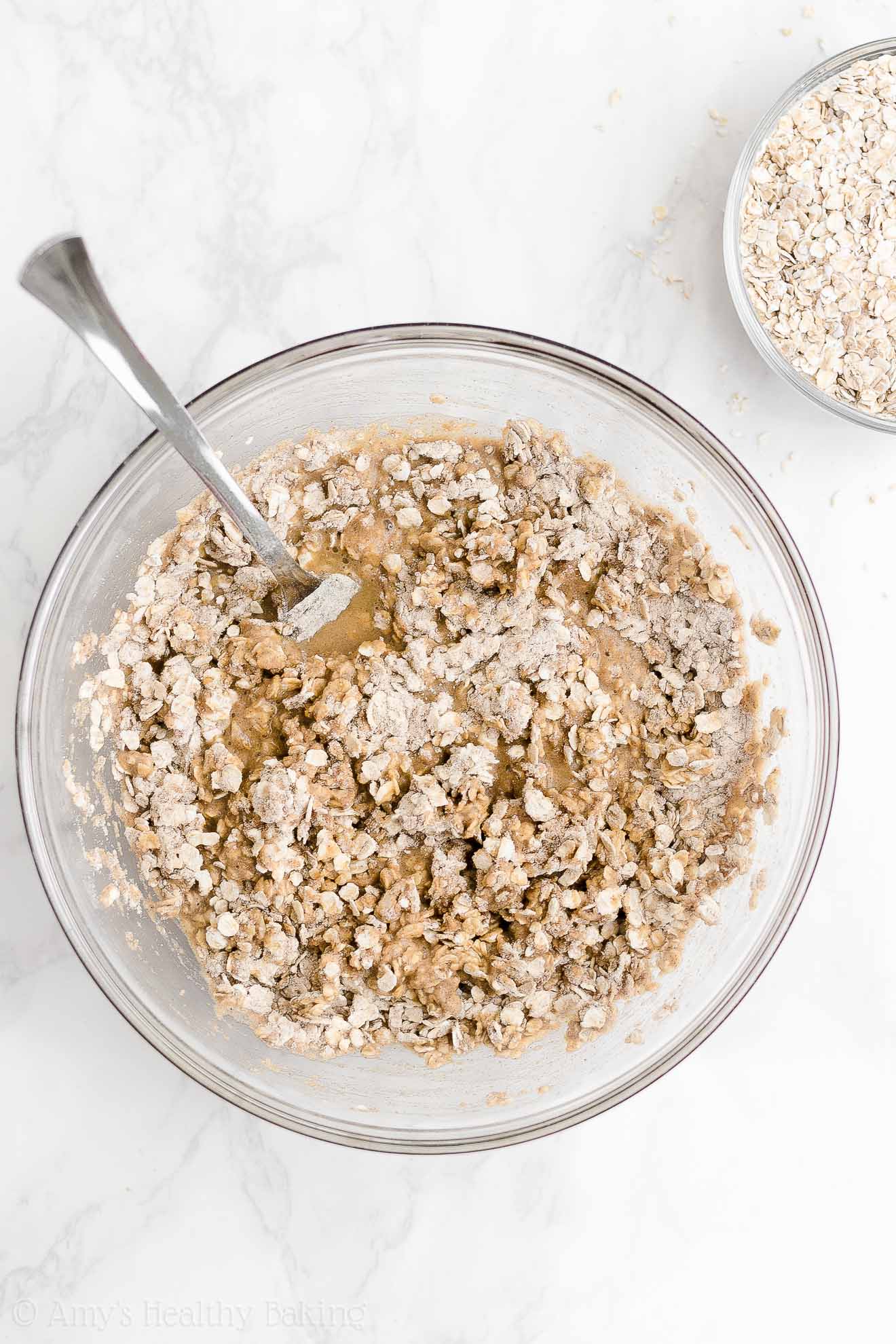 glass bowl holding a fork and the barely mixed ingredients used to make healthy strawberry oatmeal breakfast cookies – easy strawberry breakfast cookies recipe – soft, chewy, low calorie, low fat, and clean eating with whole wheat, gluten free, dairy free, and nut free options – made with oats, fresh strawberries, pure maple syrup, and no refined sugar