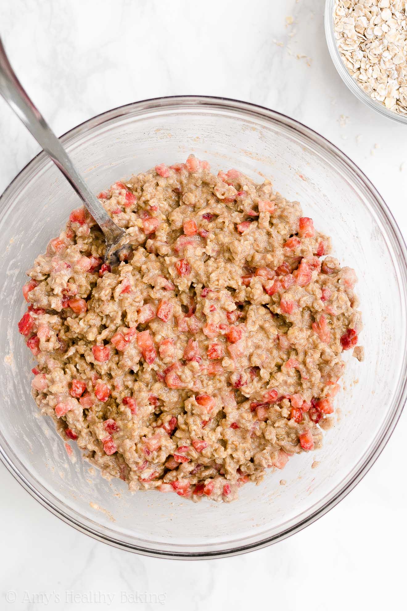 glass bowl holding a fork and the freshly stirred dough used to make healthy strawberry oatmeal breakfast cookies – easy strawberry breakfast cookies recipe – soft, chewy, low calorie, low fat, and clean eating with whole wheat, gluten free, dairy free, and nut free options – made with oats, fresh strawberries, pure maple syrup, and no refined sugar