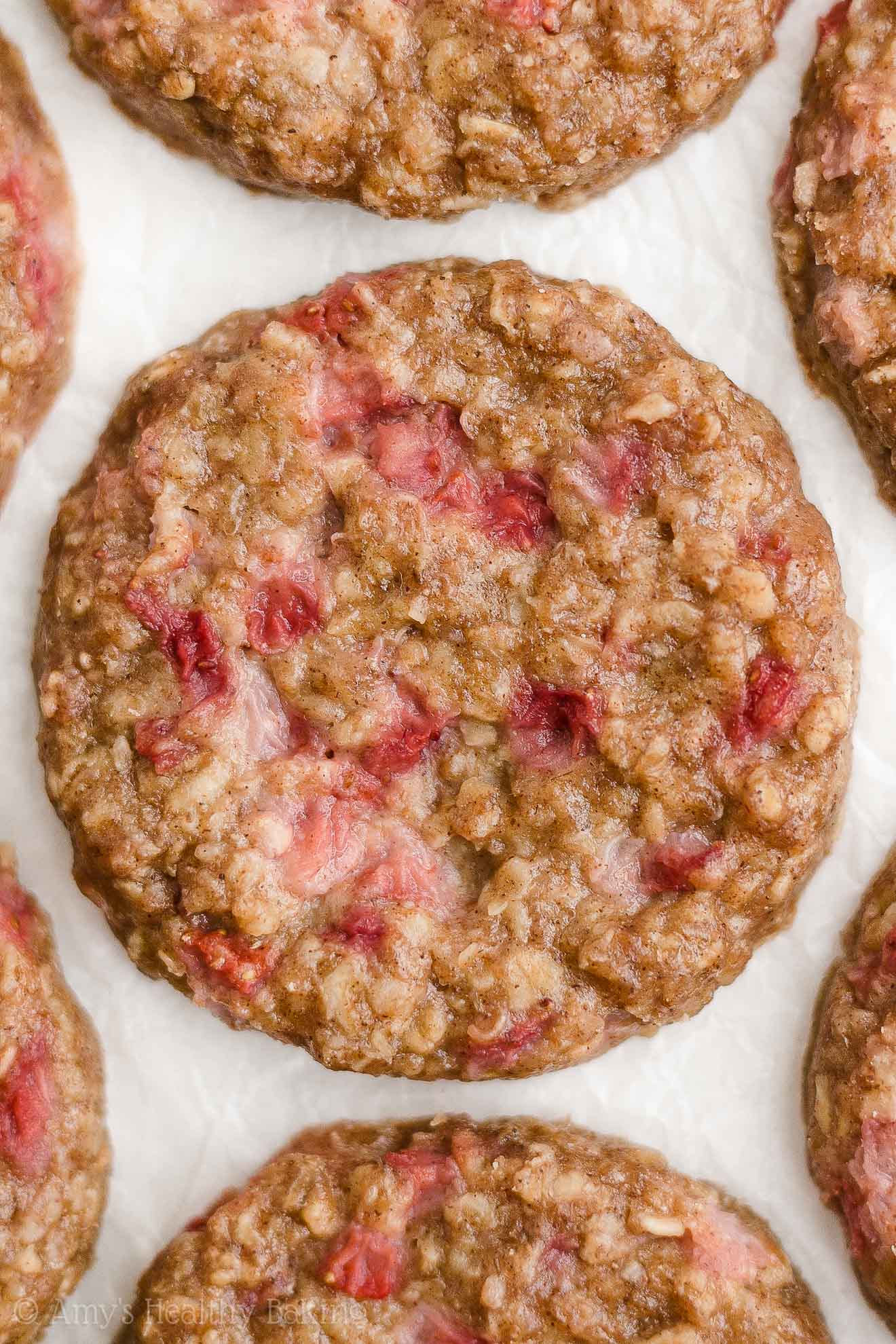 healthy strawberry oatmeal breakfast cookies on white parchment paper – easy strawberry breakfast cookies recipe – soft, chewy, low calorie, low fat, and clean eating with whole wheat, gluten free, dairy free, and nut free options – made with oats, fresh strawberries, pure maple syrup, and no refined sugar