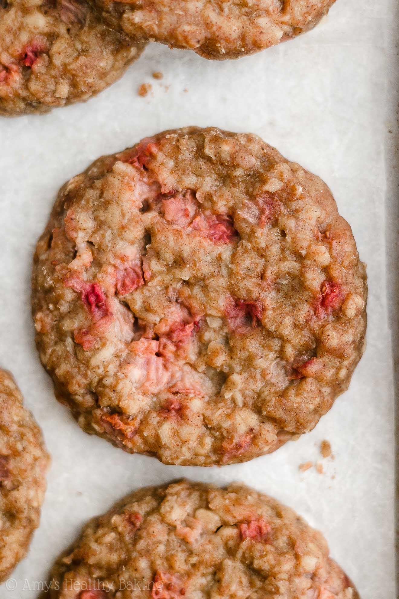 freshly baked healthy strawberry oatmeal breakfast cookies on a baking sheet lined with white parchment paper – easy strawberry breakfast cookies recipe – soft, chewy, low calorie, low fat, and clean eating with whole wheat, gluten free, dairy free, and nut free options – made with oats, fresh strawberries, pure maple syrup, and no refined sugar